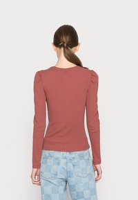 Langärmliges geripptes Oberteil in gedecktem Rosaton mit gepufften Schultern, kombiniert mit blauen karierten Jeans, von hinten betrachtet.