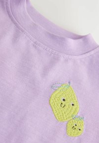 Fliederfarbenes T-Shirt mit zwei bestickten gelben Zitronen mit lächelnden Gesichtern und blauen Akzenten, aus weichem Baumwollstoff gefertigt.