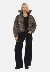 Kurtka puchowa w panterkę z wysokim kołnierzem, długimi rękawami i zapięciem na zamek z przodu. Zestawiona z czarnymi spodniami w szerokim kroju i masywnymi czarnymi botkami.