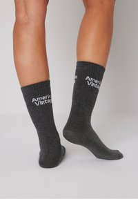 Pilkas raukšlėtas kojines su baltais užrašais "American Vintage" priekyje. Dizainas yra iki vidurio blauzdos, su minkšta tekstūra.