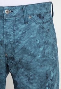 Light blue denim pants with a textured surface, featuring a button closure and subtle stitching details along the pockets and seams.