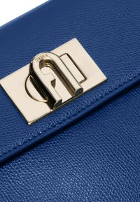 Blauwe leren handtas met textuur, voorzien van een goudkleurige metalen sluiting en een gladde stiksels langs de randen.