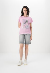 Pink short-sleeve t-shirt with a graphic design featuring flowers and the word "glow." Paired with gray denim shorts and white sneakers.