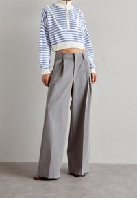 Persona che indossa pantaloni larghi grigi e una maglia a righe blu e bianca corta con collo alto e cerniera.