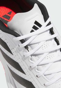 White athletic shoe with black accents, featuring a textured upper, white laces, and a red inner lining with a logo displayed.