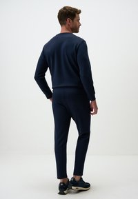 Navyblaues Sweatshirt- und Jogginganzug-Set, hergestellt aus weichem Stoff. Die Jogginghose verfügt über eine Gesäßtasche und schmal zulaufende Beine, kombiniert mit dunklen Sneakers.