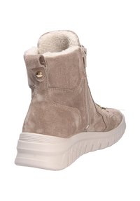 Bottines en daim beige avec une semelle texturée blanche, une fermeture éclair latérale et une doublure en fourrure au col, présentant des accents décoratifs en or.