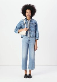 Casaco de denim azul claro com botões, usado sobre uma blusa cinza, combinado com jeans azul claros de cintura alta e mocassins pretos. Pequena mala branca.