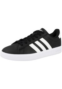 Zapatilla deportiva negra con diseño de tres franjas blancas, parte superior sintética lisa, punta redonda, suela blanca plana y cordones negros.