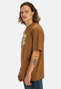 Braunes Baumwoll-T-Shirt mit kurzen Ärmeln und Rundhalsausschnitt, mit einem grafischen Druck auf der Vorderseite und einer lockeren Passform.