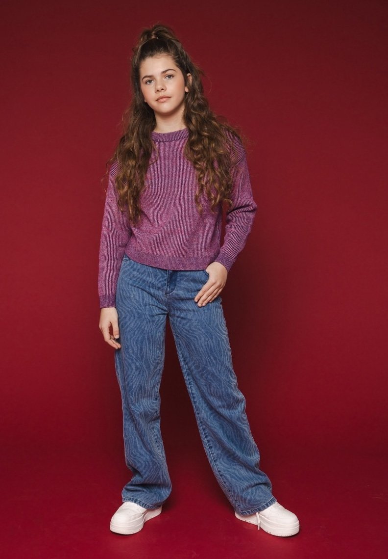 Paars gestructureerd sweatshirt, blauwe denim broek met een zebra-patroon en witte platform schoenen. Eenvoudig, casual ontwerp tegen een rode achtergrond.