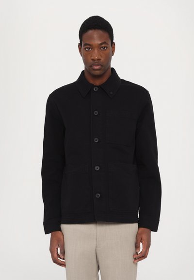 Veste noire en tissu robuste, dotée d'un col, de boutons à l'avant, de deux grandes poches et d'une texture légère. Design simple et fonctionnel.