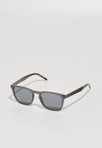 Ochelari de soare gri, rectangulari, cu lentile colorate, având o finisare mată și un model texturat pe brațe. Logo-ul "HUGO" în roșu.