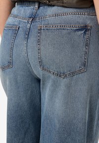 Light blue denim jeans with a high waistband, featuring two back pockets and visible stitching details. Soft texture with a relaxed fit.
