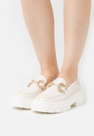 Cremfarbene Loafers mit einer massiven weißen Sohle, versehen mit einer goldenen Kettenakzentuierung über dem Blatt. Aus glattem Leder und mit minimalistischem Design.