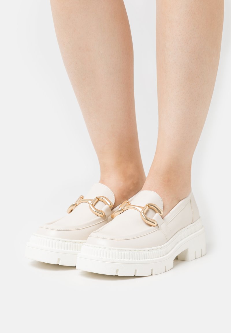 Krémové loafers s robustnou bielou podrážkou, s pozláteným reťazovým akcentom cez vrch. Hladký kožený materiál a minimalistický dizajn.