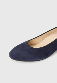 Tummansininen mokkanahkainen ballerina-malli, jossa on pyöristetty kärki ja kevyt reuna, varustettuna ohuella mustalla ommelluilla reunuksilla aukon ympärillä.