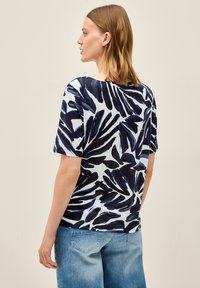 Camiseta de manga corta con un patrón de hojas azul y marino sobre un fondo azul claro, hecha de una tela suave y con un corte holgado.