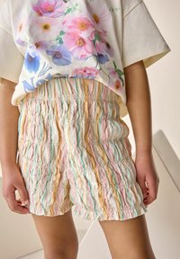 Shorts élastiques de couleur pastel avec un tissu texturé plissé, présentant des rayures roses, jaunes et bleues. Convient pour un usage quotidien.