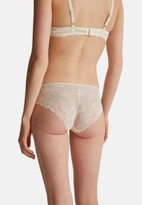 Lingerie in pizzo color off-white, con un motivo floreale e bordi scallopati. Il retro mostra dettagli in pizzo e una texture delicata.