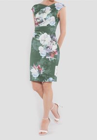 Grøn floral kjole med korte ærmer, tætsiddende design, markeret talje, prydet med store hvide og pink blomster, parret med hvide stroppehæle.