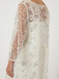 Λευκό φόρεμα από λευκή δαντέλα με διαφανή μακριά μανίκια, διακοσμημένο με ασημένιες παγιέτες και λεπτομέρειες από χάντρες. Μαλακό, υφασματοποιημένο ύφασμα με περίπλοκα σχέδια.