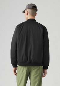 Svart bomberjacka med en slät yta, ribbat krage och muddar samt elastisk midja. Matchas med olivgrönt byxor.