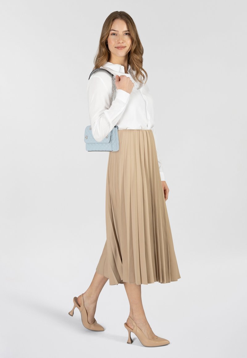 Gonna beige plissettata, camicia bianca con bottoni, borsa trapuntata blu chiaro e décolleté beige. Tessuti morbidi e colori tenui.