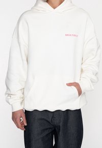 Witte hoodie met een voorzak en een capuchon met trekkoord. Voorzien van roze tekst "MULTIPLY" op de borst. Zachte stof met geribbelde boorden.
