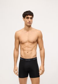 Czarne bokserki z miękkiego, elastycznego materiału i elastycznym pasem w talii z logo "Calvin Klein" w kolorze białym.