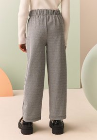 Pantalones a cuadros en blanco y negro con cintura elástica, que presentan un corte holgado y perneras anchas, combinados con zapatos negros gruesos.