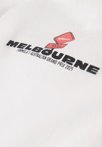 Biała bawełniana koszulka z czarnym nadrukiem "MELBOURNE" oraz czerwoną grafiką z napisem "NEXT APPEARANCE" nad "FORMULA 1 AUSTRALIAN GRAND PRIX 2025."