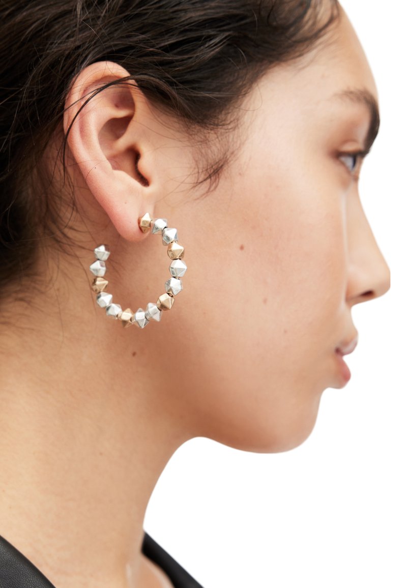 Hoop earrings featuring alternating geometric silver and gold-tone metal accents, with a textured surface and a rounded shape.