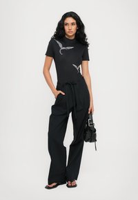 Black fitted t-shirt with bird design and rhinestones, paired with loose black high-waisted trousers. Accessories include a studded handbag.