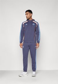 Conjunto de sudadera y pantalones de chándal en color navy con acentos en azul claro y naranja. Presenta un logo bordado y rayas laterales. Textura de tela suave.