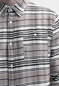 Camicia a quadri grigia e bianca con colletto, dotata di taschino sul petto e bottoni circolari. Tessuto morbido con un motivo a trama.