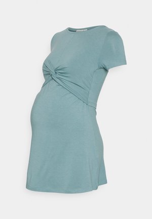 Robe de maternité bleu clair à manches courtes avec un détail de nœud torsadé sous la poitrine, présentée sur un mannequin sur fond blanc.