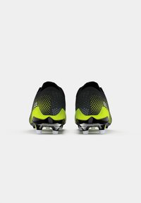 Chuteiras pretas e amarelas neon com um cabedal texturizado, design aerodinâmico e cravos brancos numa sola preta, enfatizando a aderência para um desempenho superior.