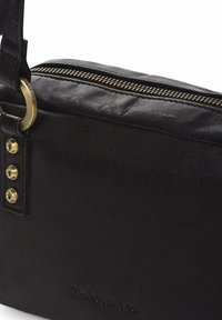 Bolso de cuero negro con cremallera en tono dorado, herrajes redondos y cinco remaches decorativos en el lateral. Textura suave, forma rectangular.