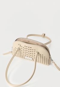 Μικρή μπεζ δερμάτινη τσάντα χειρός με διάτρητο μπροστινό μέρος, ασημένιο φερμουάρ, δύο λαβές και αποσπώμενο ιμάντα ώμου σε λευκό φόντο.