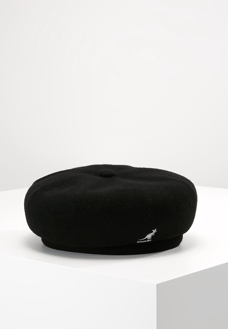 Béret en laine noire avec un petit logo kangourou brodé près du bord, présenté sur un socle blanc sur un fond uni.