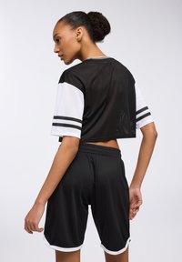 Top corto in rete nera con maniche bianche e pantaloni corti neri. Il top presenta strisce laterali e un motivo testurizzato. I pantaloni corti hanno un accento bianco all'orlo.