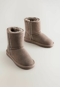 Botas de tobillo de ante marrón con forro de piel sintética, que presentan una costura lateral decorativa y una suela de goma texturizada para mayor agarre.