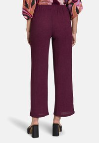 Pantalons larges pliss�és bordeaux avec une taille élastique, fabriqués en tissu léger, offrant un aspect texturé.