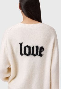 Sweter w kolorze kremowym, z mieszanki wełny, z czarnym, puszystym napisem „love” na plecach. Okrągły dekolt i luźny krój z opuszczonymi ramionami.
