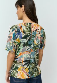 Blouse à manches courtes à motif floral avec un mélange de teintes vertes, roses et bleues. Fermeture à boutons au dos avec un design à fente au centre. Matière en mélange de coton.