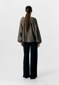 Blouse à motifs marron foncé avec des manches ballon, associée à un pantalon noir à jambes larges. Coiffure avec de longs cheveux en queue de cheval.