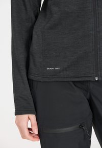 Svart snabbtorkande långärmad topp med texturerad yta. Har en dragkedja och en liten etikett med "QUICK DRY" vid fållen.