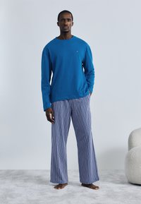 Μπλε πουκάμισο με μακριά μανίκια συνδυασμένο με άσπρο-μπλε παντελόνι φαρδύ με ρίγες. Το ύφασμα φαίνεται μαλακό· τα χρώματα είναι ζωντανά και αντιθετικά.