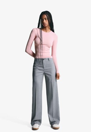 Long-sleeve pink shirt paired with wide-leg gray trousers, featuring button closure and a smooth texture, complemented by white sneakers.